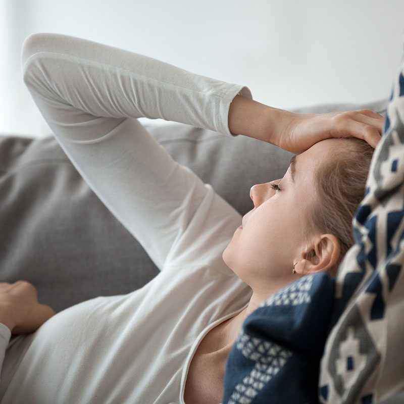 Young woman lying on couch feeling strong headache migraine