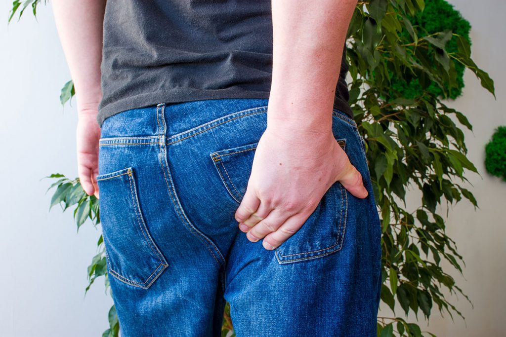Man keeps hand on lower part of buttocks.