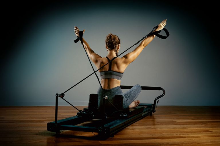 Woman doing pilates exercises with a reformer bed.