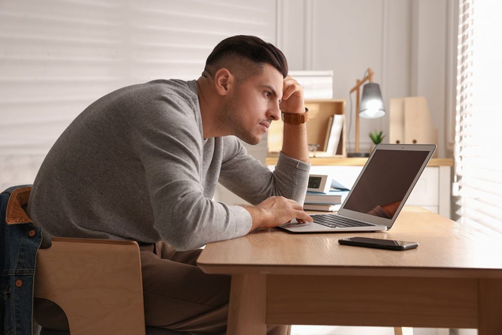 Man with poor posture using laptop at table indoors with headache